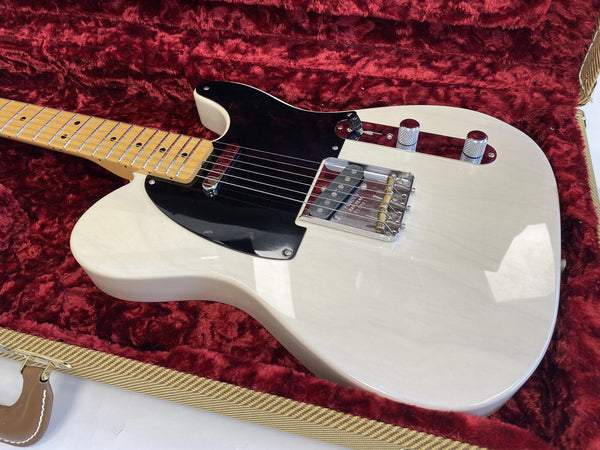 White electric guitar with black pickguard and maple neck resting in red plush-lined guitar case
