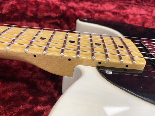 Close-up of electric guitar maple neck and fretboard with metal frets and strings on white body with black pickguard against red velvet background