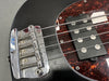 Close-up of black electric bass guitar bridge and humbucker pickup with tortoiseshell pickguard and metal strings