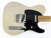 Close-up of cream electric guitar body with black pickguard, chrome bridge, control knobs, and maple neck with dot inlays