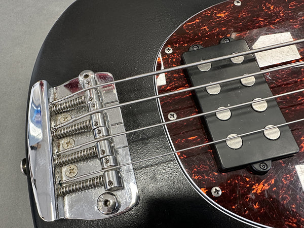 Close-up of black electric bass guitar bridge and humbucker pickup with tortoiseshell pickguard and metal strings