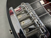 Close-up of chrome bridge and springs on black electric bass guitar with metal strings and tuning screws