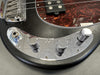 Close-up of black electric bass guitar with chrome control plate and knobs, tortoiseshell pickguard, and metal bridge on gray background