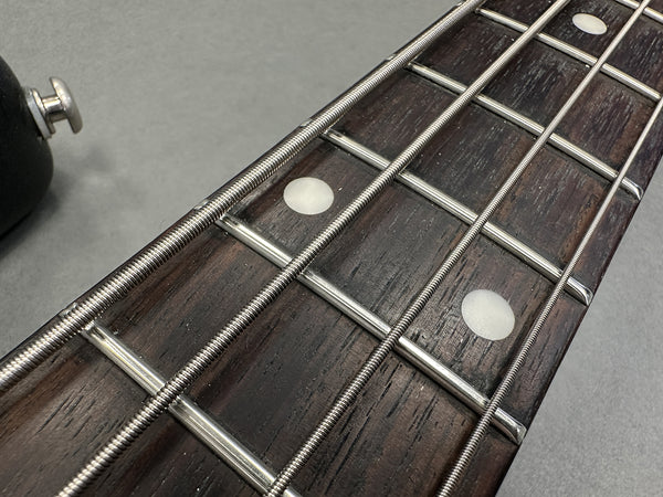 Close-up of bass guitar fretboard with metal frets, round white position markers, and wrapped steel bass strings on dark wood fingerboard