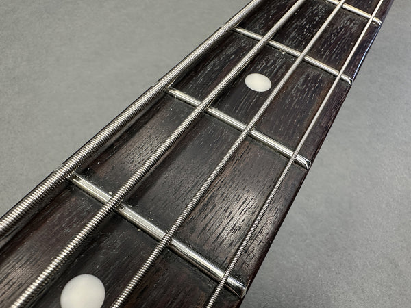 Close-up of bass guitar fretboard showing metal frets, wound strings, and dot inlays on dark wood fingerboard