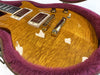 Close-up of honey burst quilted maple electric guitar body with chrome humbucker pickups and bridge inside purple plush-lined guitar case
