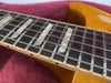 Close-up of electric guitar rosewood fretboard with mother of pearl block inlays and metal frets on a honey-colored guitar body resting on a red fabric background