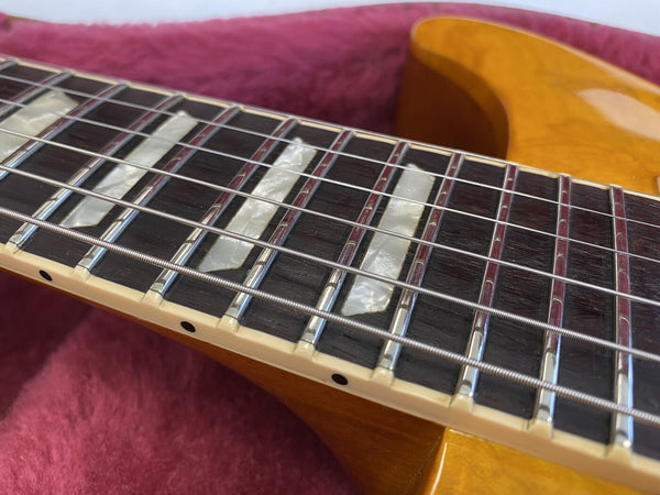 Close-up of electric guitar rosewood fretboard with mother of pearl block inlays and metal frets on a honey-colored guitar body resting on a red fabric background