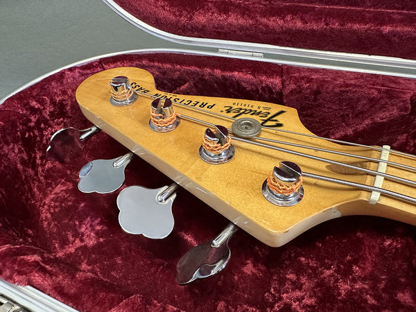 Close-up of Fender Precision Bass headstock with tuning pegs and strings inside a red velvet-lined guitar case