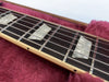 Close-up of guitar fretboard with pearl block inlays and metal strings on a plush red case lining