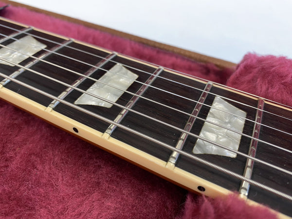 Close-up of guitar fretboard with pearl block inlays and metal strings on a plush red case lining