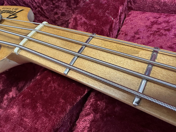 Close-up of Fender bass guitar maple neck with silver frets and strings resting on plush red velvet guitar case interior