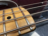 Close-up of electric bass guitar strings and frets on a light wood fingerboard with black dot marker and black body finish