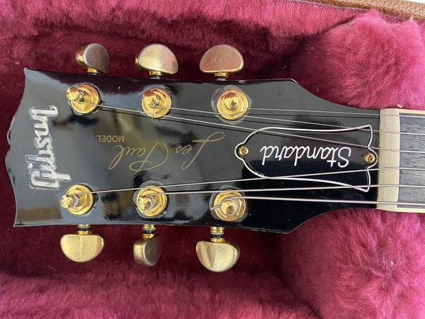Close-up of Gibson Les Paul Standard guitar headstock with gold tuning pegs and truss rod cover on red plush case lining