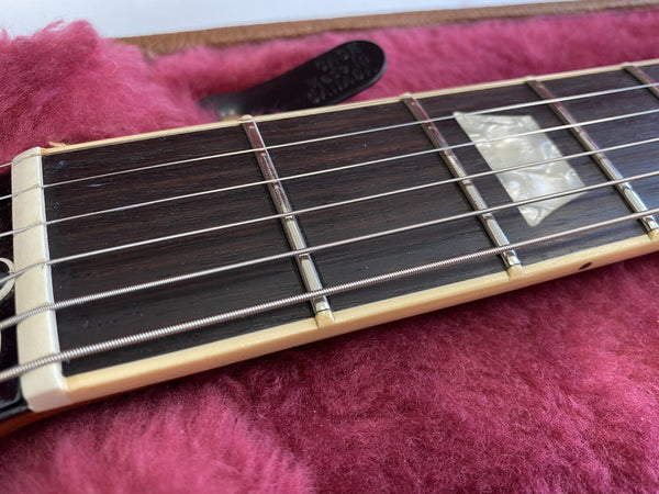 Close-up of guitar fretboard with metal frets, mother-of-pearl inlay, and strings on pink plush case lining
