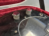 Close-up of black electric guitar control knobs and input jack on scratched pickguard inside red velvet-lined guitar case