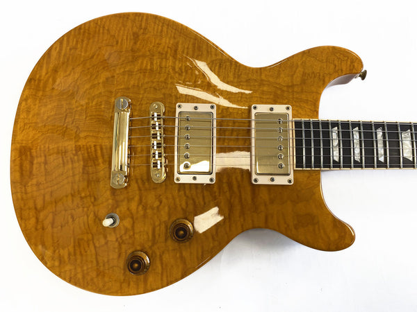 Honey burst electric guitar with quilted maple top, gold humbucker pickups, two control knobs, and toggle switch on light background