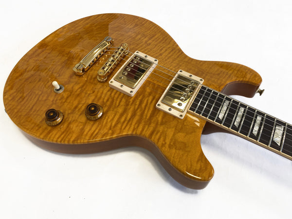 Electric guitar with honey amber quilted maple top, gold hardware, two humbucker pickups, and rosewood fretboard with block inlays on white background