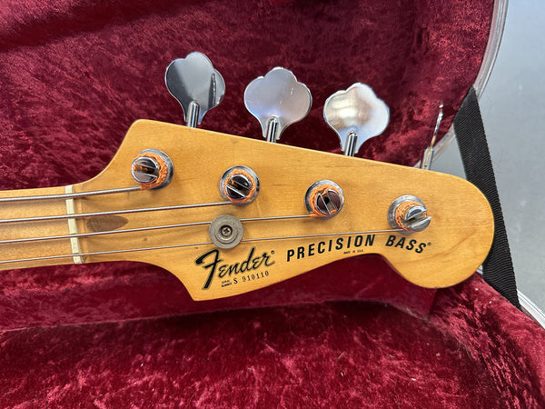 Close-up of Fender Precision Bass headstock with tuning pegs and strings on red velvet guitar case lining