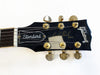Close-up of black Gibson Les Paul Standard guitar headstock with gold tuning pegs and white logo on a white background