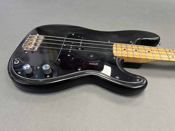 Black electric bass guitar with maple neck and fretboard, showing body and control knobs on gray background