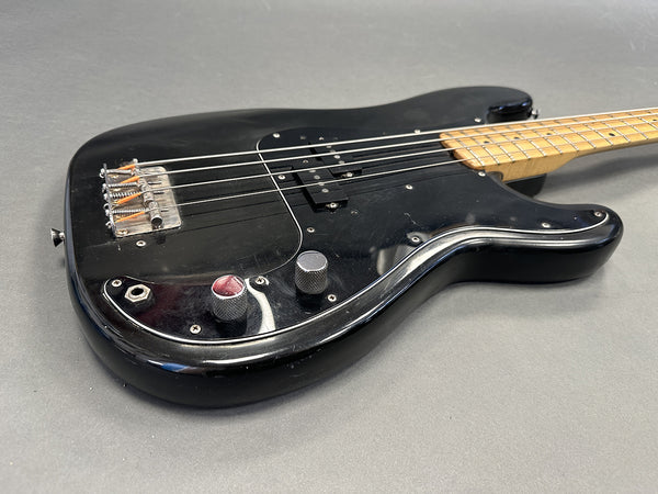 Black electric bass guitar with a maple neck and metal control knobs on a gray background