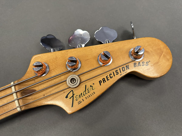 Close-up of Fender Precision Bass guitar headstock with tuning pegs and serial number on natural wood finish