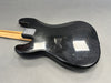 Black electric guitar body with visible scratches and wear, maple neck with a dual stripe, laid on gray surface showing metal neck plate with guitar logo.