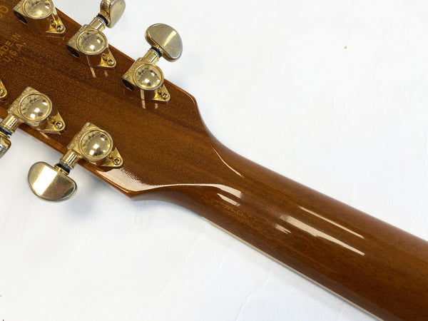 Close-up of the back of a glossy finished wooden guitar neck with gold Grover tuning pegs on a white background.