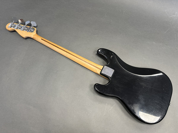 Black electric bass guitar with maple neck and chrome tuning pegs, rear view showing Fender neck plate and worn body finish