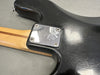 Close-up of black electric guitar body showing worn finish, engraved metal neck plate with four screws, and maple neck with walnut stripe on gray background.