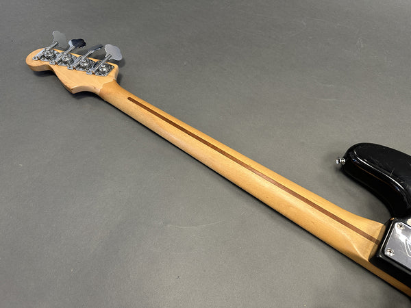 Back of maple bass guitar neck with chrome tuning pegs and black body edge on gray background