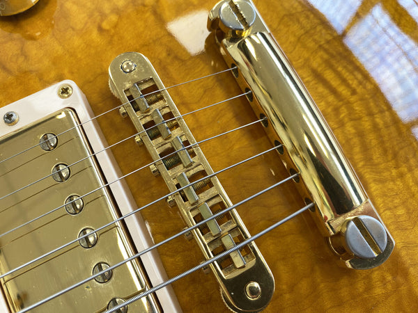 Close-up of gold Tune-o-Matic bridge and tailpiece on honey burst electric guitar with metal humbucker pickup and steel guitar strings