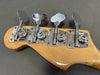 Close-up of Fender bass guitar tuning pegs on natural wood headstock against gray background