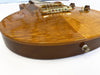 Close-up of a glossy amber quilted maple top electric guitar body with gold hardware and control knobs on white background