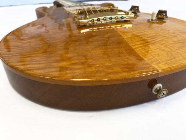 Close-up of a glossy amber quilted maple top electric guitar body with gold hardware and control knobs on white background