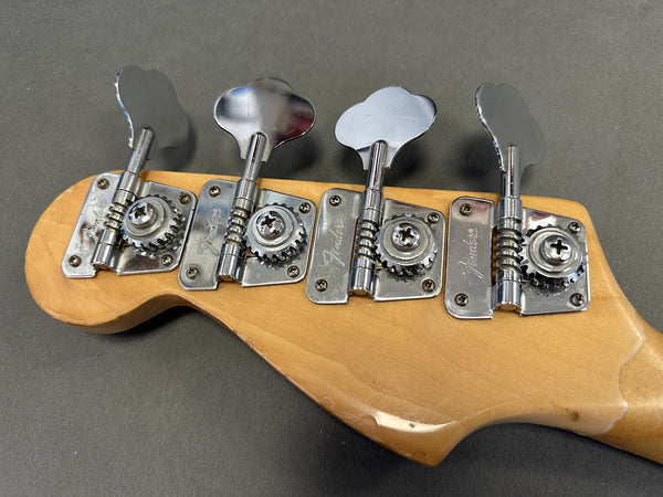 Close-up of Fender bass guitar tuning pegs on natural wood headstock against gray background