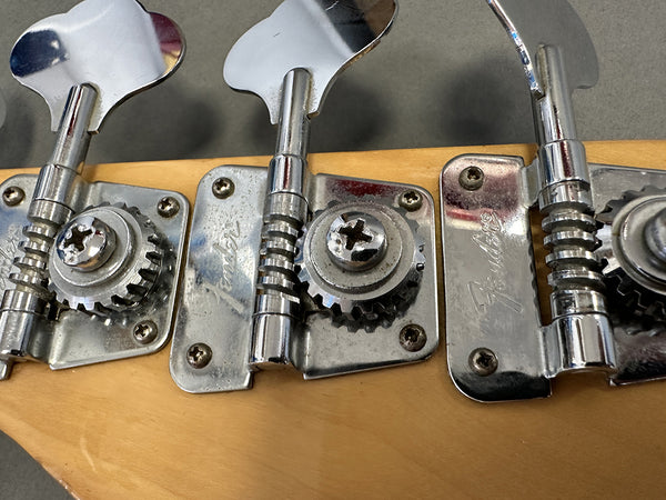Close-up of vintage Fender bass guitar tuning pegs with chrome finish on a natural wood headstock