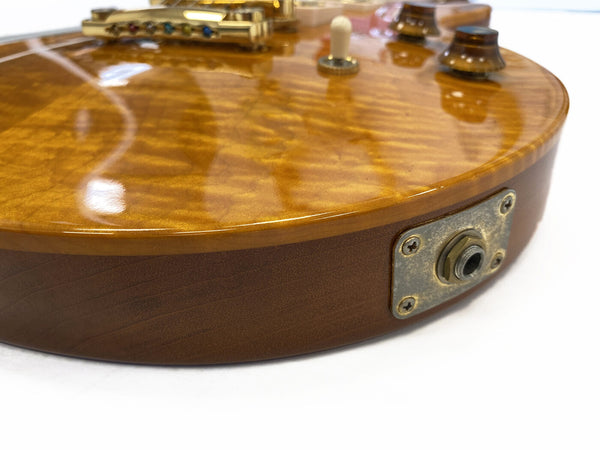 Close-up of electric guitar body with quilted maple top finish, gold hardware, toggle switch, control knob, and vintage-style output jack plate