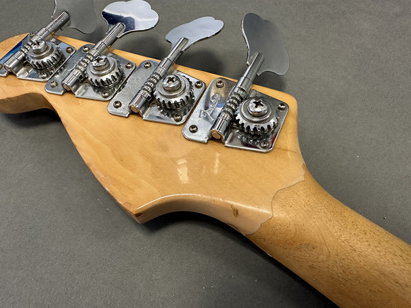 Close-up of natural wood finish Fender bass guitar headstock with chrome tuning pegs and worn edges on gray background