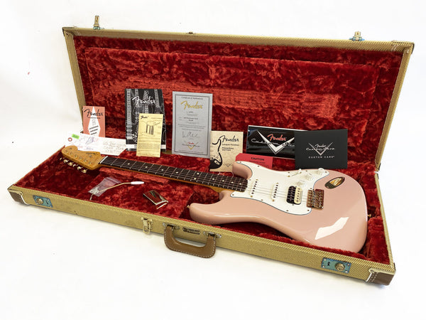 Fender Stratocaster electric guitar in pink with white pickguard inside open vintage tweed case lined with red velvet, accompanied by Fender manuals, certificate of authenticity, tremolo arm, and metal bridge cover