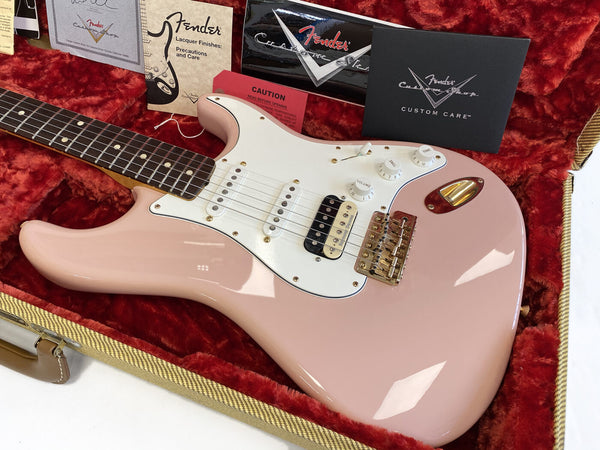 Fender Custom Shop electric guitar in pink with white pickguard and gold hardware, displayed in a red plush-lined case with Fender care booklets and certificates