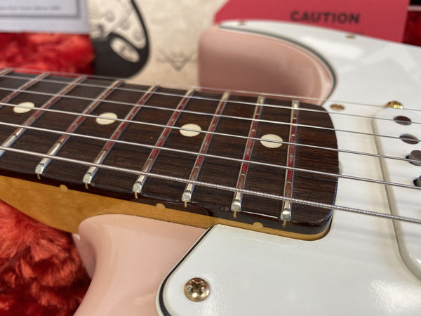 Close-up of electric guitar rosewood fretboard with dot inlays and metal frets, showing white and pink guitar body with strings and pickguard screws, displayed on red plush surface for sale at Coffee House Guitars.