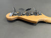 Close-up of natural wood electric bass guitar headstock with four chrome tuning pegs on gray background