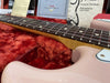 Close-up of pink electric guitar neck and fretboard with dot inlays resting on red plush case lining with Fender care pamphlets in background