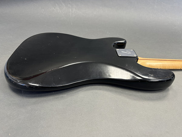 Black electric guitar body back with visible scratches and wear, maple neck attached, placed on gray surface