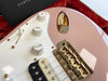 Close-up of pink electric guitar body showing white tone and volume knobs, gold bridge, and pickup selector switch on white pickguard with red velvet case lining background.