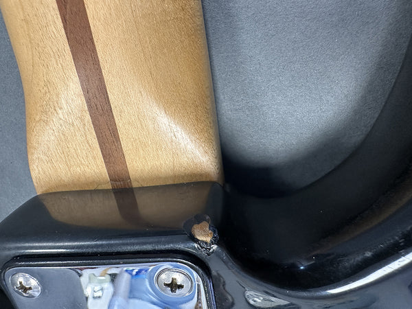 Close-up of guitar neck joint showing wood and black finish with visible chip and damage near metal plate screws