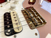 Close-up of electric guitar bridge with gold saddles, Seymour Duncan pickups, volume knob, and pink guitar body surface reflection