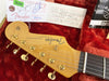 Close-up of Fender Stratocaster guitar headstock with gold tuning pegs and original Fender tags in red plush-lined case